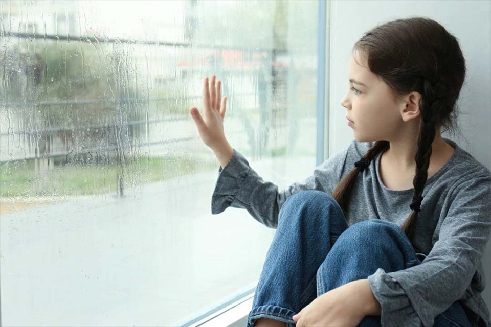 Young person looking out of a rainy window with a pensive expression