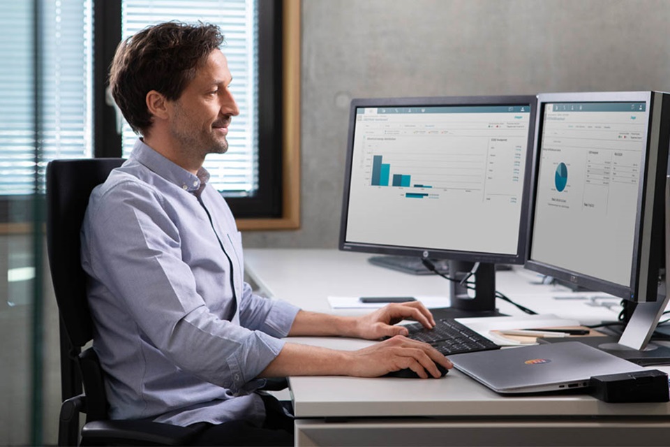 Employee working with dual monitor setup and laptop in an office environment