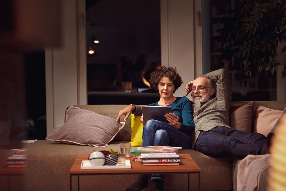 A couple relaxing on a sofa using a tablet in a cozy living room with warm lighting