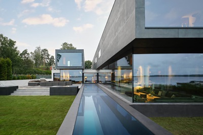 Modern luxury house with large windows, outdoor pool, and lake view at dusk